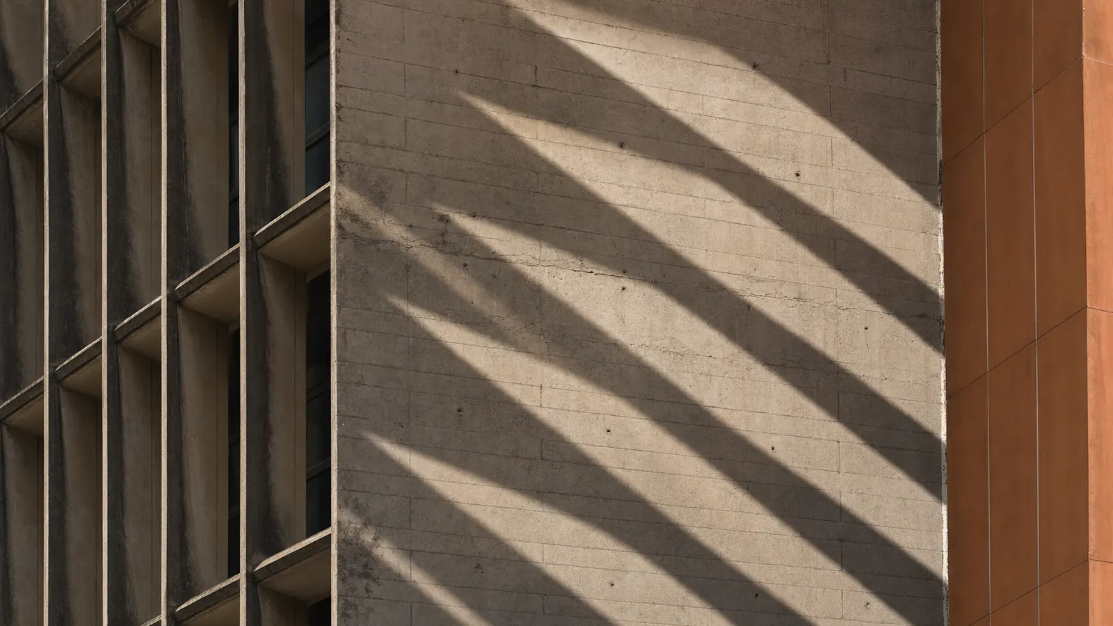 Mur de béton brut d'une tour du Plateau, traversé par les lames d'ombre des brise-soleil, panneau de terre cuite au bord.
